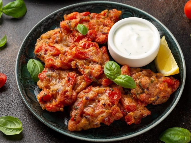 Ein schwarzer Teller mit Tomatokeftedes und einem Dip.