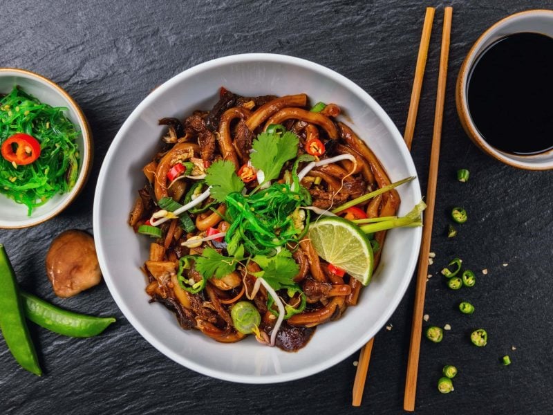 Eine weiße Schüssel mit Udon-Nudeln in Limetten-Sojasauce.