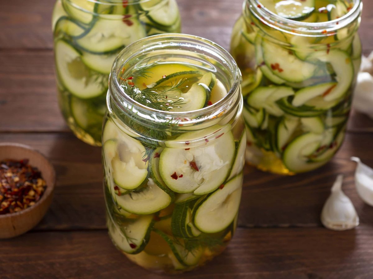 Eingelegte Zucchini7, in Scheiben geschnitten eingemacht in einer Mischung aus Essig, Kräutern und Chili, geöffnet serviert auf einem Holzbrett.