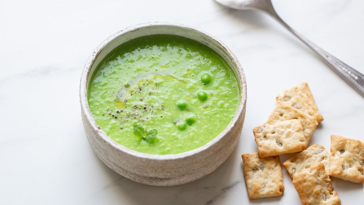 Eine Schüssel Erbsen-Kartoffelsuppe, daneben liegen Cracker und ein Löffel.