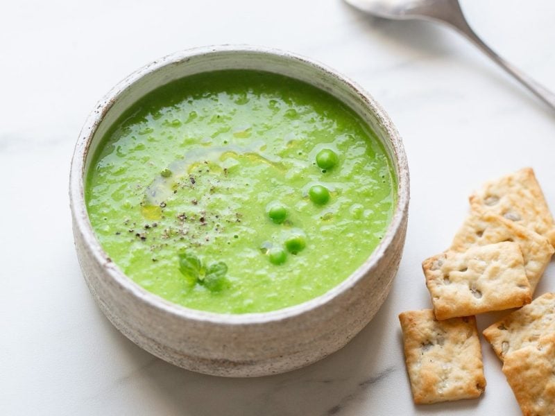 Eine Schüssel Erbsen-Kartoffelsuppe, daneben liegen Cracker und ein Löffel.