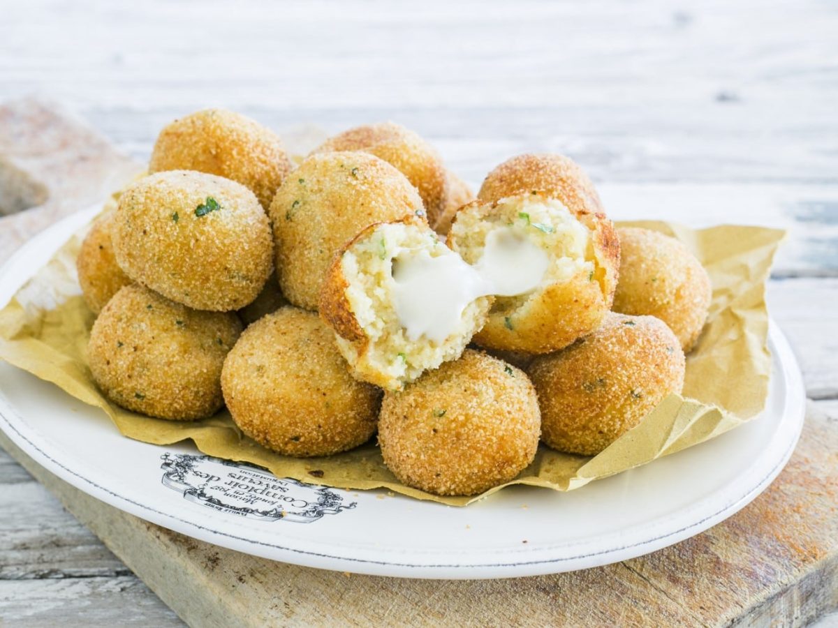 Frittierte Kartoffelbällchen mit Käsefüllung auf einem weißen Teller. Der Teller steht auf einem Holzbrett.