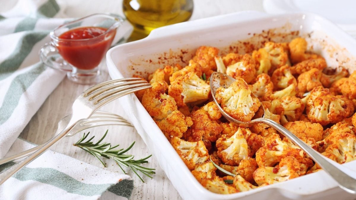 Eine Auflaufform gebackener Blumenkohl mit Tomatensauce, darin ein Löffel.