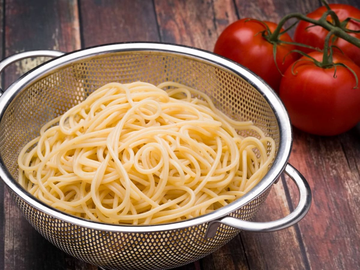 Gekochte Nudeln einfrieren: ein Sieb mit gekochten Nudeln, daneben Tomaten.