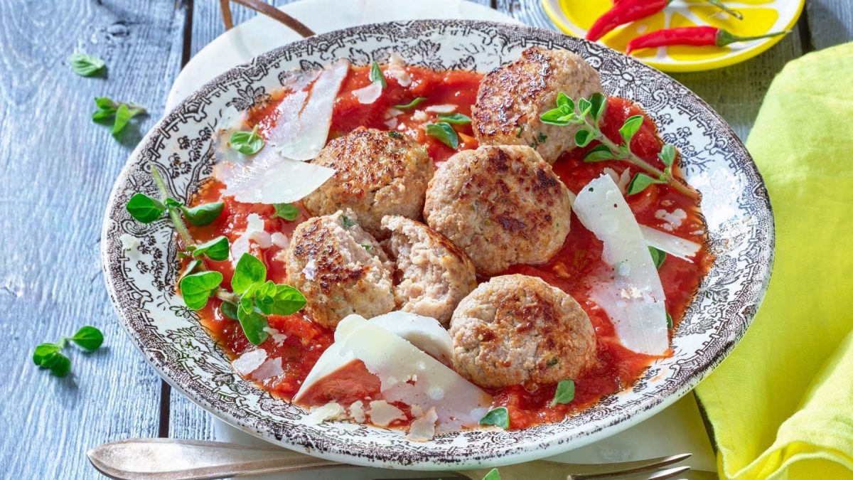 Hackbällchen mit Ricotta in würziger Tomatensauce auf einen gemusterten Teller.