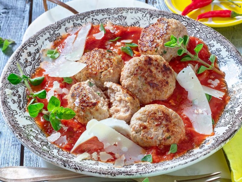 Hackbällchen mit Ricotta in würziger Tomatensauce auf einen gemusterten Teller.