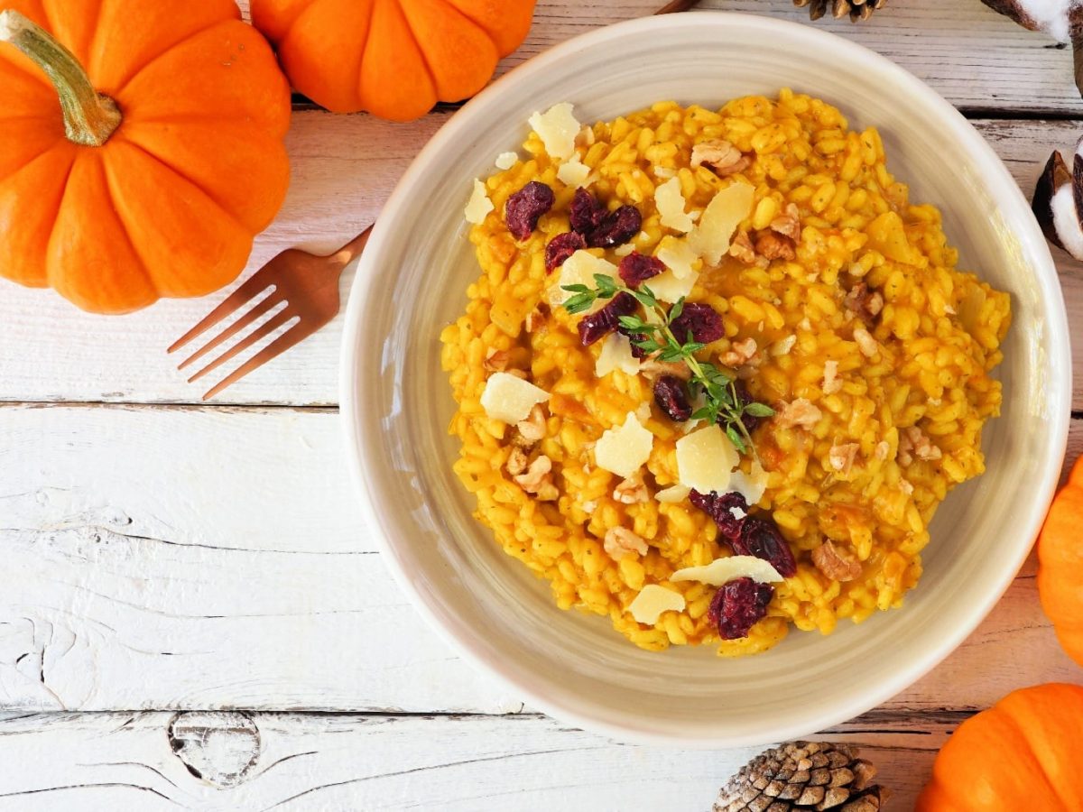 Ein weißer Teller mit dem Herbst-Risotto auf einem weißen Tisch mit allerhand herbstlicher Dekoration.