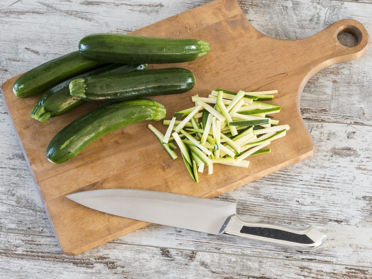 Julienne schneiden von Zucchini auf einem Holzbrett.