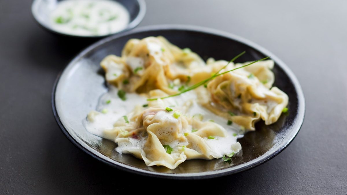 Krabben-Ravioli in Weißweinsauce auf einem dunklen Teller.