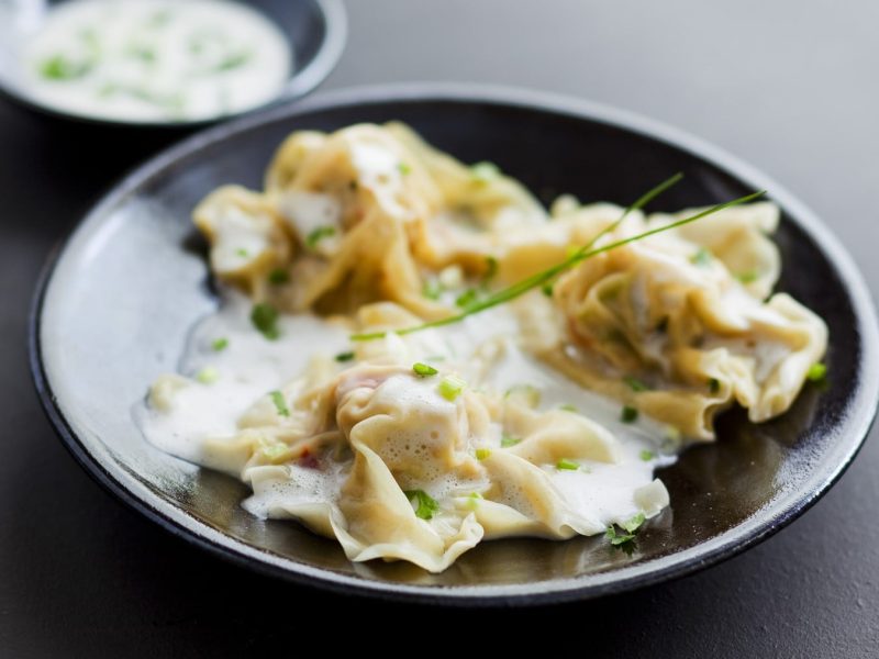 Krabben-Ravioli in Weißweinsauce auf einem dunklen Teller.