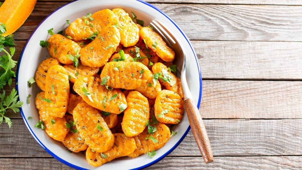 Eine Schüssel Kürbis-Gnocchi mit Petersilie bestreut, darin eine Gabel, Draufsicht.