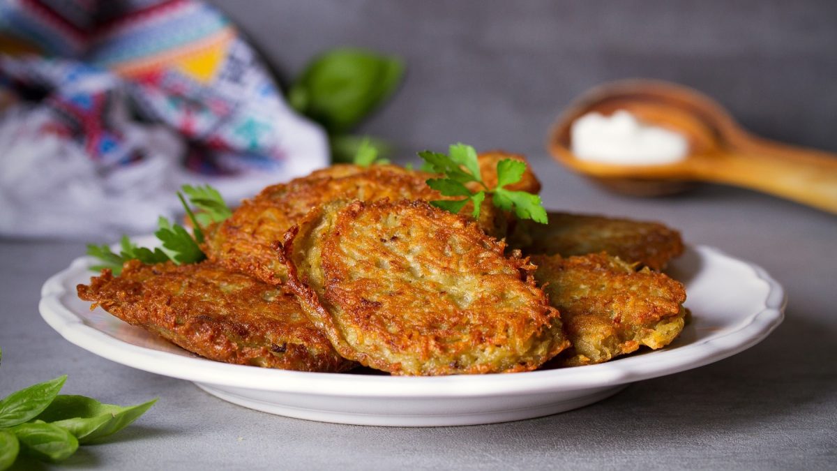 Ein Teller Kürbis-Kartoffelpuffer mit frischen Kräutern.