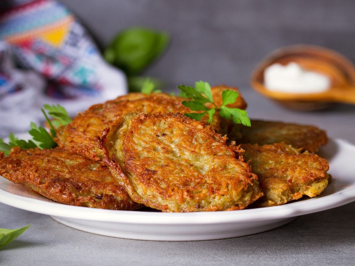 Ein Teller Kürbis-Kartoffelpuffer mit frischen Kräutern.