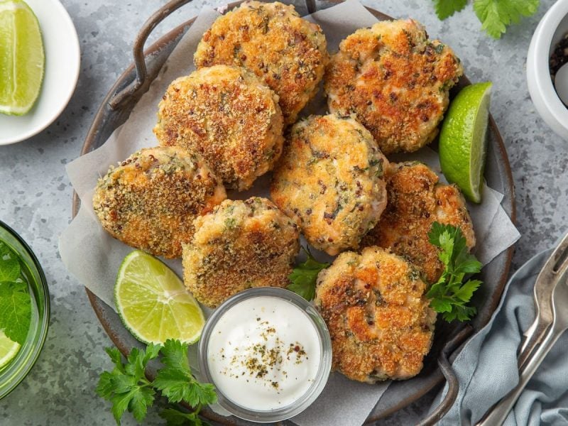 Ein Teller mit Lachs-Quinoa-Patties, frischen Limetten und einem Dip.