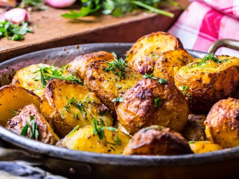 Eine Auflaufform Melting Potatoes, mit Kräutern bestreute gebackene Kartoffelstücke.