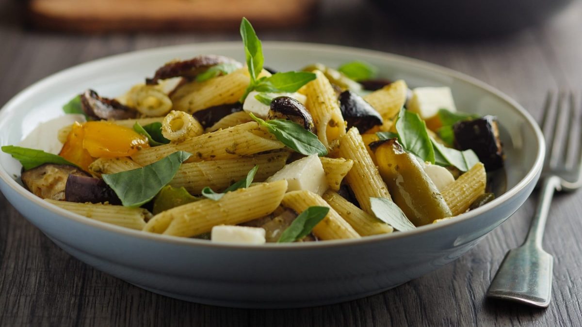 Ein tiefer Teller Pasta-Auberginensalat mit Basilikum, daneben liegt eine Gabel.