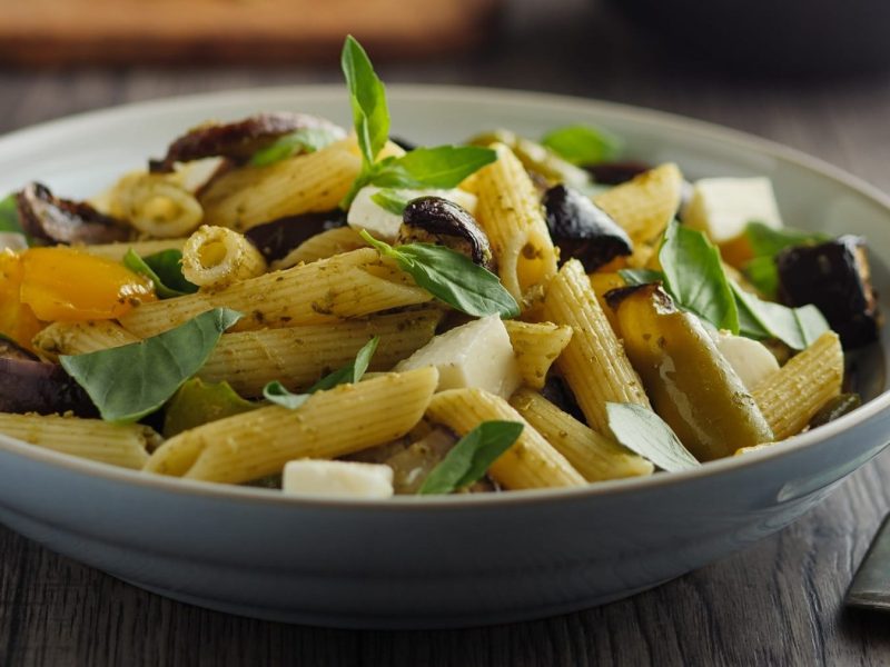 Ein tiefer Teller Pasta-Auberginensalat mit Basilikum, daneben liegt eine Gabel.