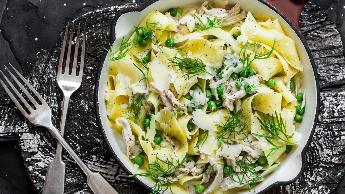 Pappardelle mit Fenchel, Erbsen und Hähnchen in cremiger Sauce auf Teller und schwarzem Untergrund. Daneben zwei Gabeln. Draufsicht.