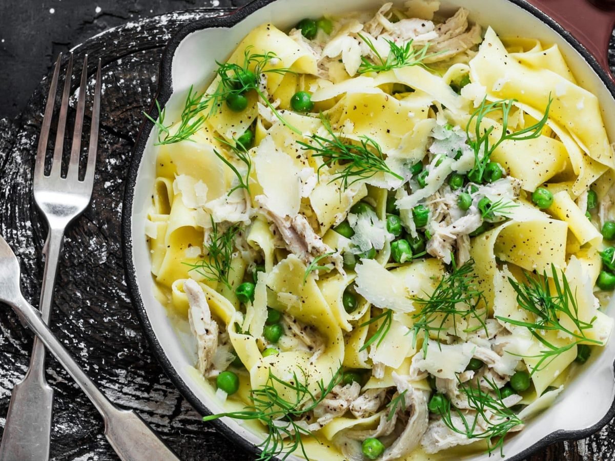 Pappardelle mit Fenchel, Erbsen und Hähnchen in cremiger Sauce auf Teller und schwarzem Untergrund. Daneben zwei Gabeln. Draufsicht.