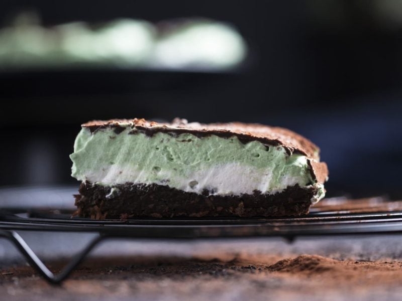 Ein Stück Schokoladen-Minzcreme-Kuchen auf einem Gitter vor dunklem Hintergrund.