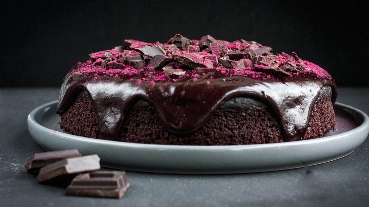 Schoko-Rote-Bete-Kuchen mit Himbeerpulver und Schokostücken garniert auf einem Teller vor dunklem Hintergrund.