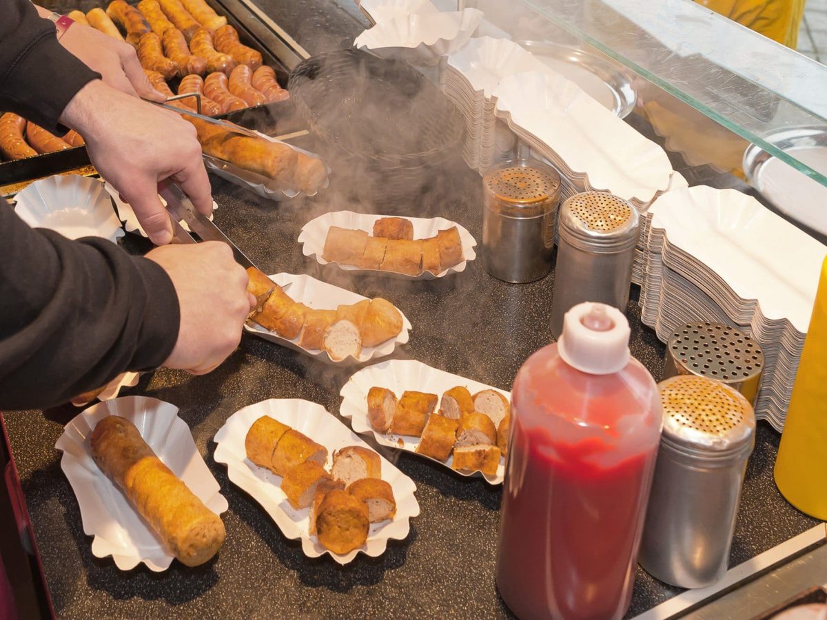 Tag der Currywurst Mann bereitet Currywürste zu. Im Bild Würste, Saucen, Pappschalen und Kochplatte. Draufsicht.