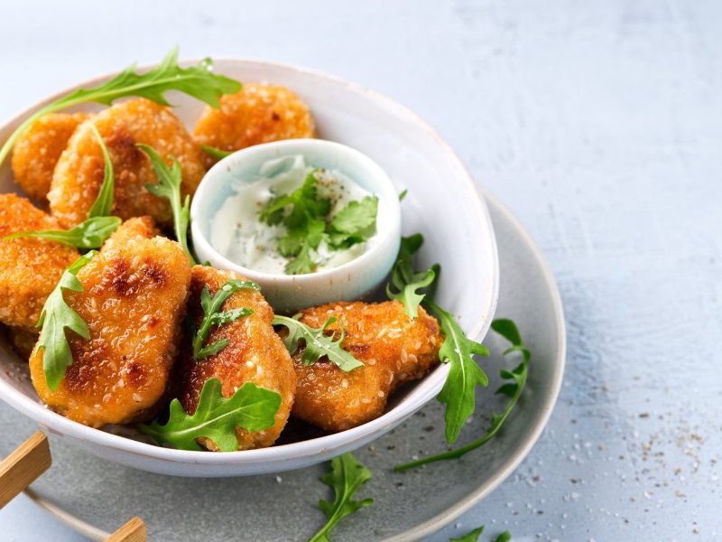 Eine Schale panierte Tempeh Nuggets mit einem Dip in der Mitte.