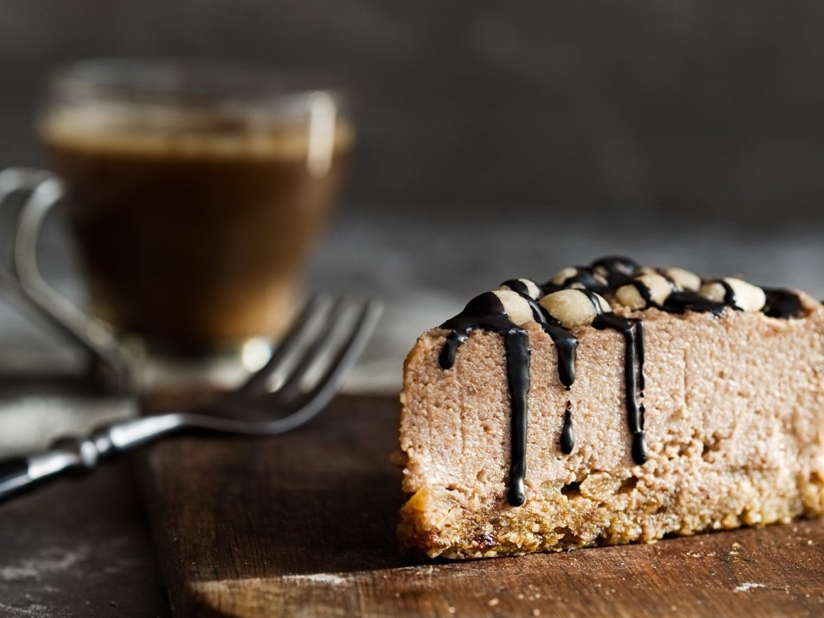 Ein Stück veganer Schoko-Cheesecake, daneben eine Gabel und eine Tasse Kaffee.