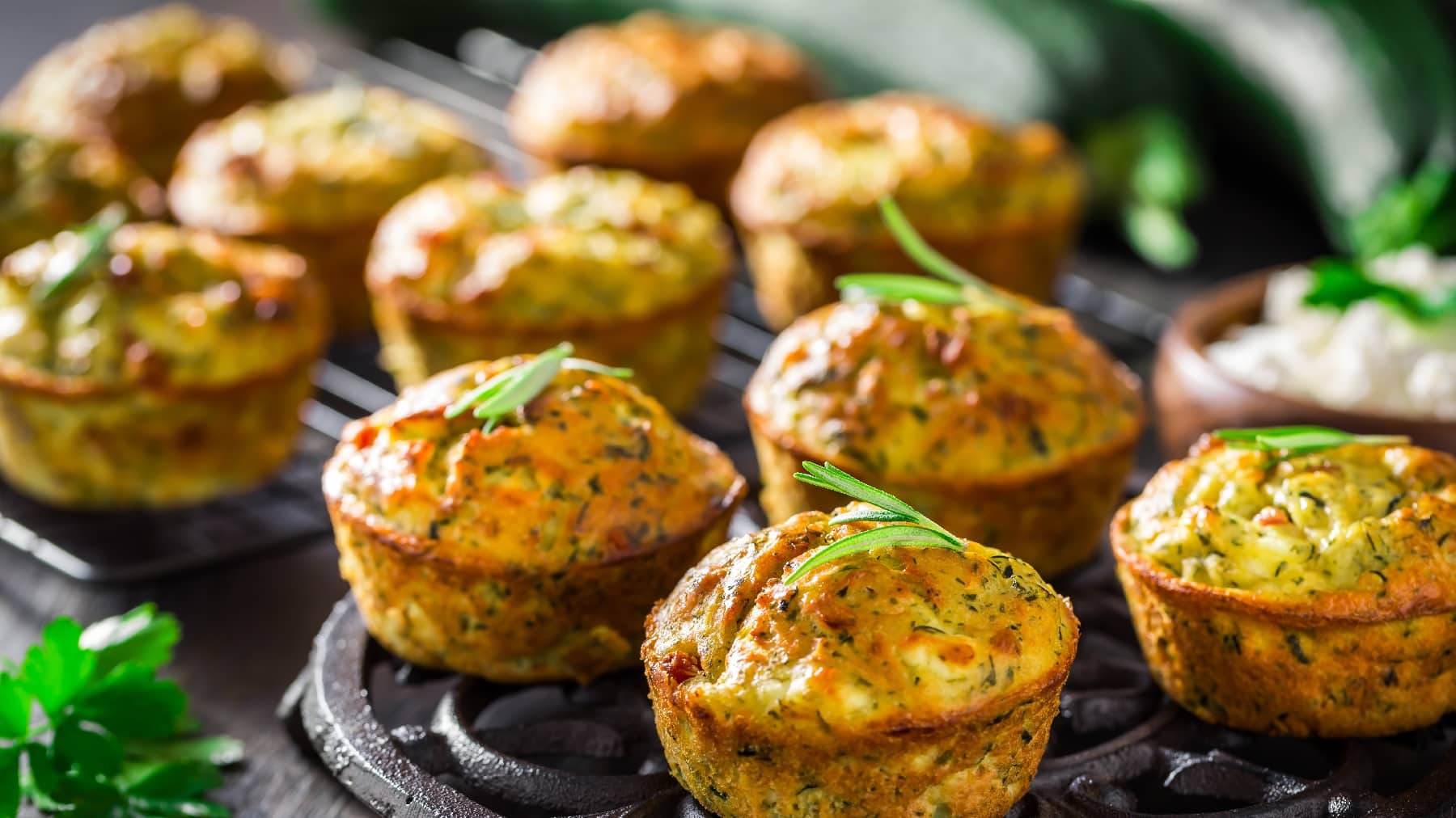 Mehrere der Zucchini-Muffins auf einem Blech mit Kräutern dekoriert.