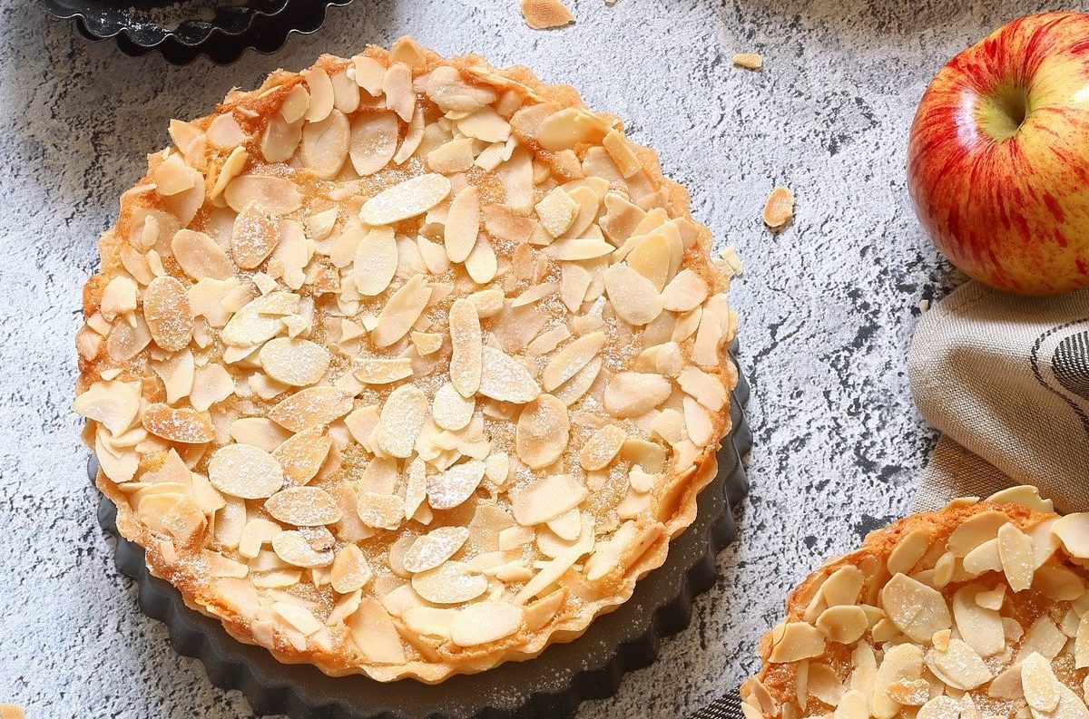 Apfel-Schüttelkuchen mit Mandeln auf grauer Oberfläche.