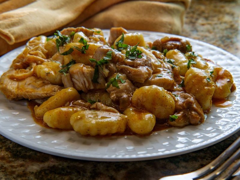 Gnocchi-Gulasch-Topf auf weißem Teller auf Marmor. Daneben liegt Besteck.