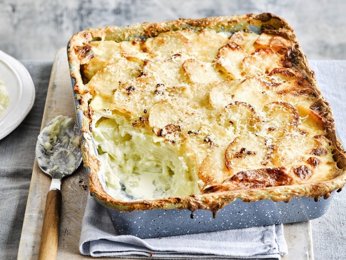 Gratin Dauphinois, mit dünn geschnittenen Kartoffelscheiben und einer dicken Schicht gratiniertem Käse, serviert in einer großen Auflaufform auf einem rustikalen Brett.