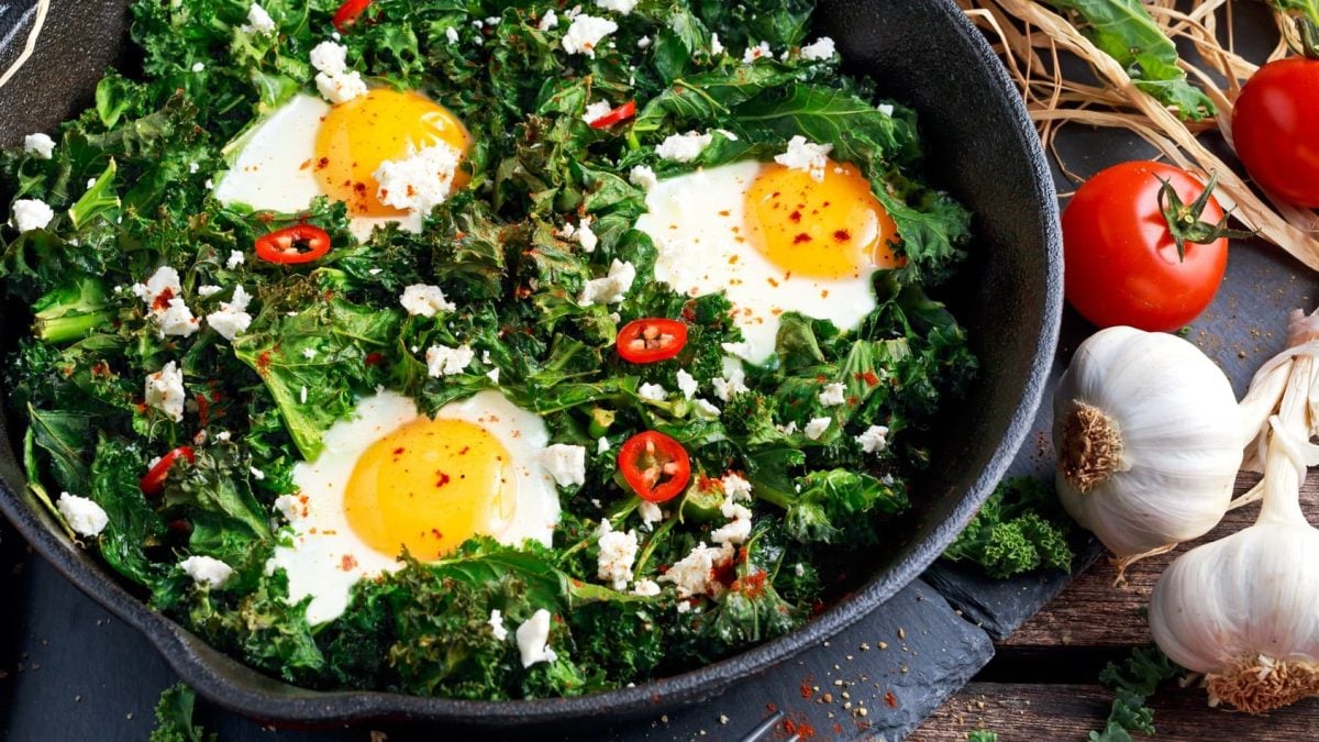 Grünkohlpfanne mit Feta, Spiegelei und Chili auf Schieferplatte.