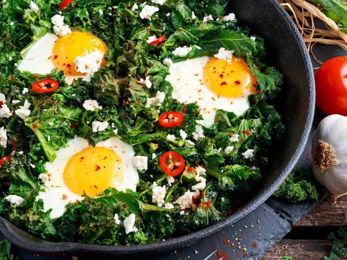 Grünkohlpfanne mit Feta, Spiegelei und Chili auf Schieferplatte.