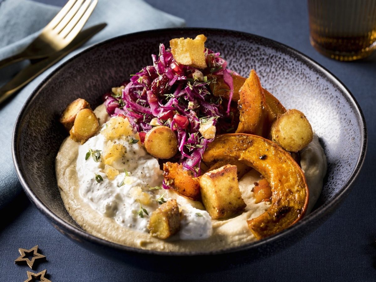 Mezze mit gebackenem Kürbis, Fetacreme, Hummus, Rotkohlsalat und knusprigem Brezelcrunch, serviert in einer dunklen Keramikschale.