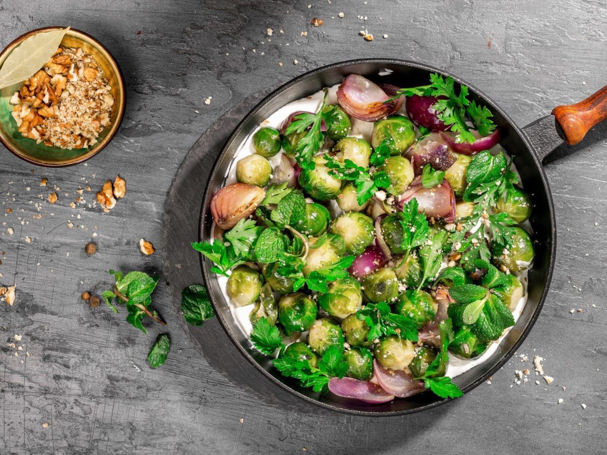 Rosenkohlpfanne mit frischer Joghurt-Limetten-Sauce auf grauem Untergrund.