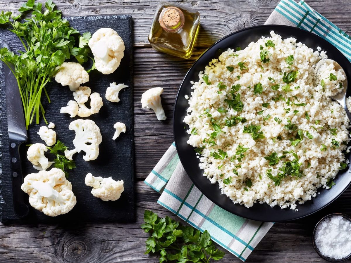 Ein Teller Blumenkohl-Reissalat mit Petersilie bestreut in der Draufsicht, daneben Limettenspalten.