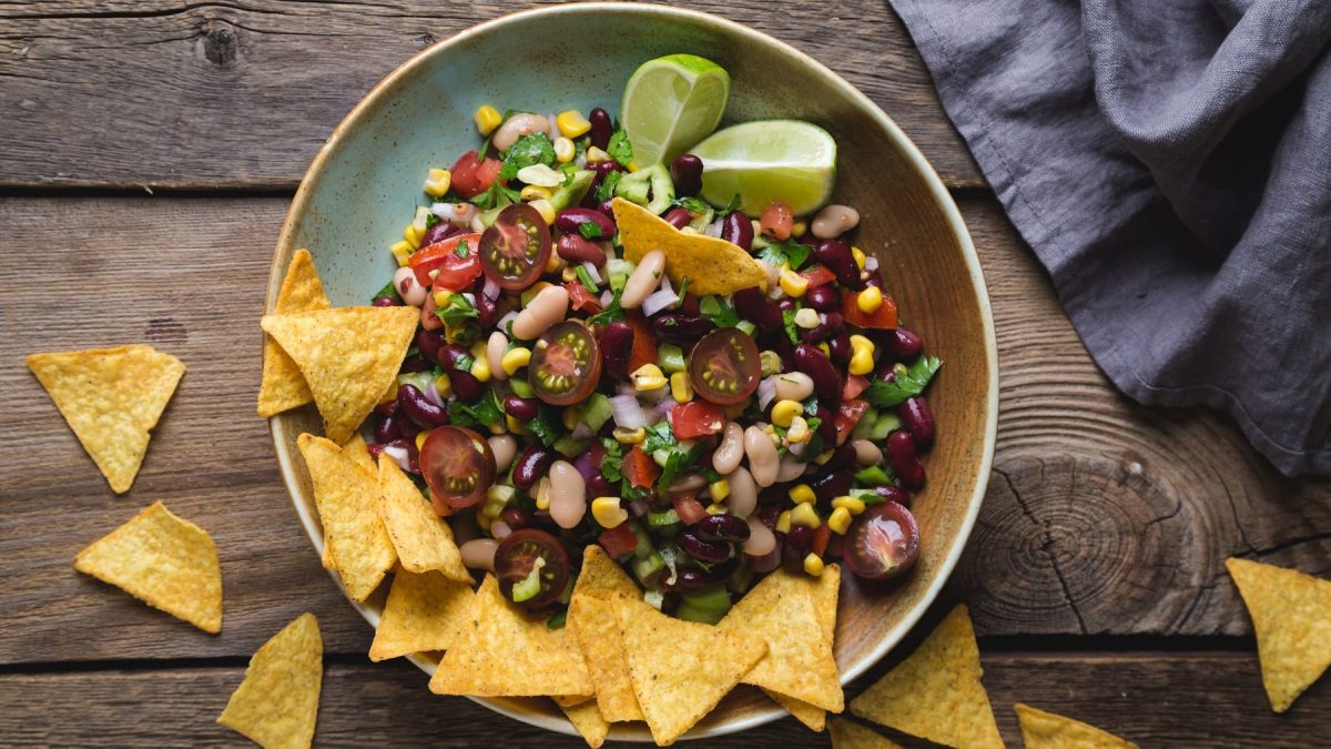 Eine Schale Cowboy Caviar, ein Dip oder Salat aus Bohnen, Tomaten, Mais, Zwiebeln und Paprika, dazu Nachos und Limettenspalten.