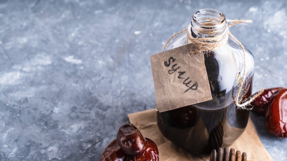 Eine Flasche Dattelsirup mit Etikett, daneben liegen Datteln.