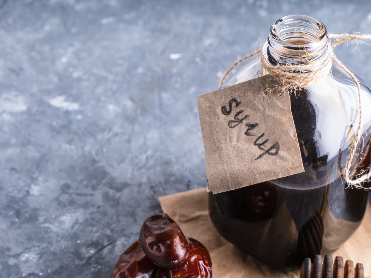 Eine Flasche Dattelsirup mit Etikett, daneben liegen Datteln.