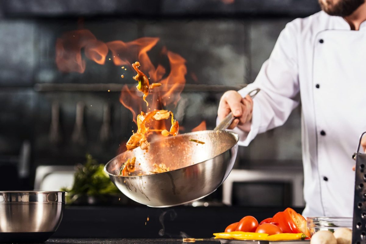 eat! Berlin 2022: Ein Koch schwenkt einen Wok, aus dem eine Flamme aufsteigt.