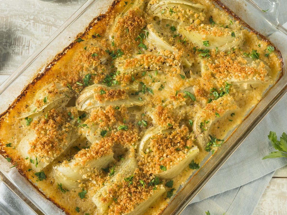 Eine gläserne Auflaufform mit Fenchel-Gratin auf einem hellgrauen Küchentuch.