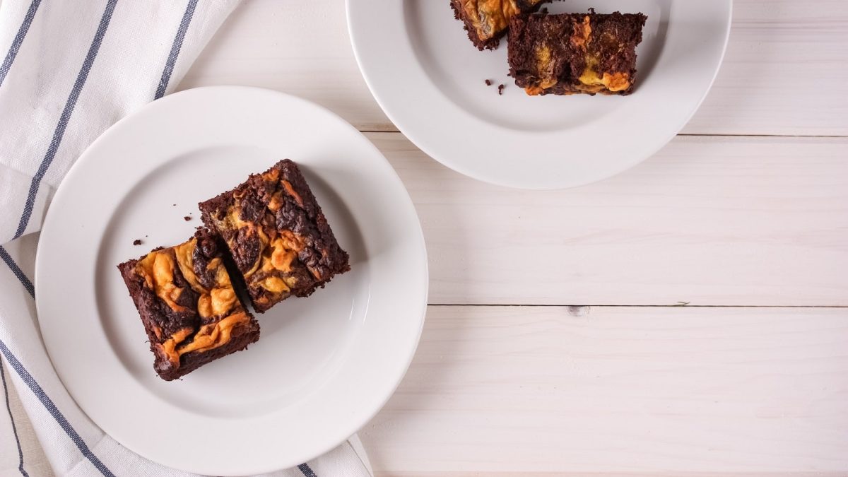 Ein weißer Teller mit Kürbis-Brownies darauf neben einem gestreiften Küchentuch.