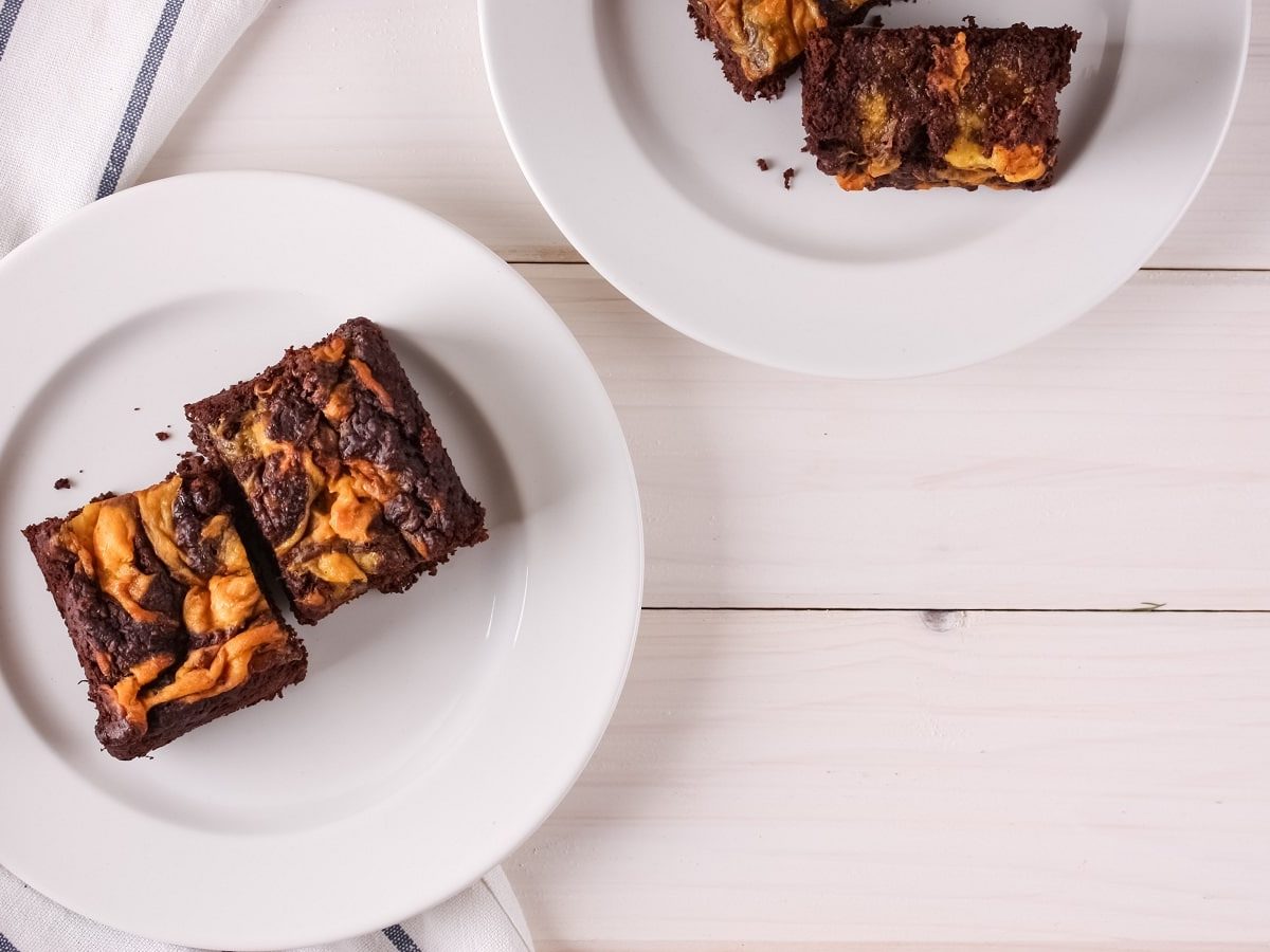 Ein weißer Teller mit Kürbis-Brownies darauf neben einem gestreiften Küchentuch.