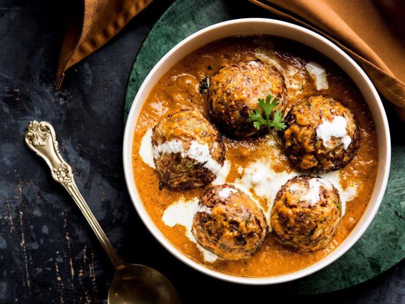 Eine weiße Schüssel mit Malai Kofta auf einem dunkelgrünen Tuch.