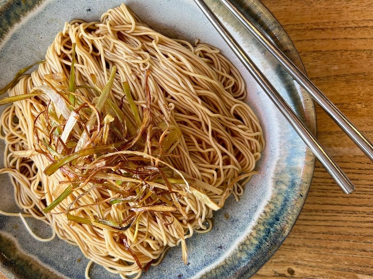 Ein Keramikteller mit Scallion Oil Noodles auf einem Holztisch.