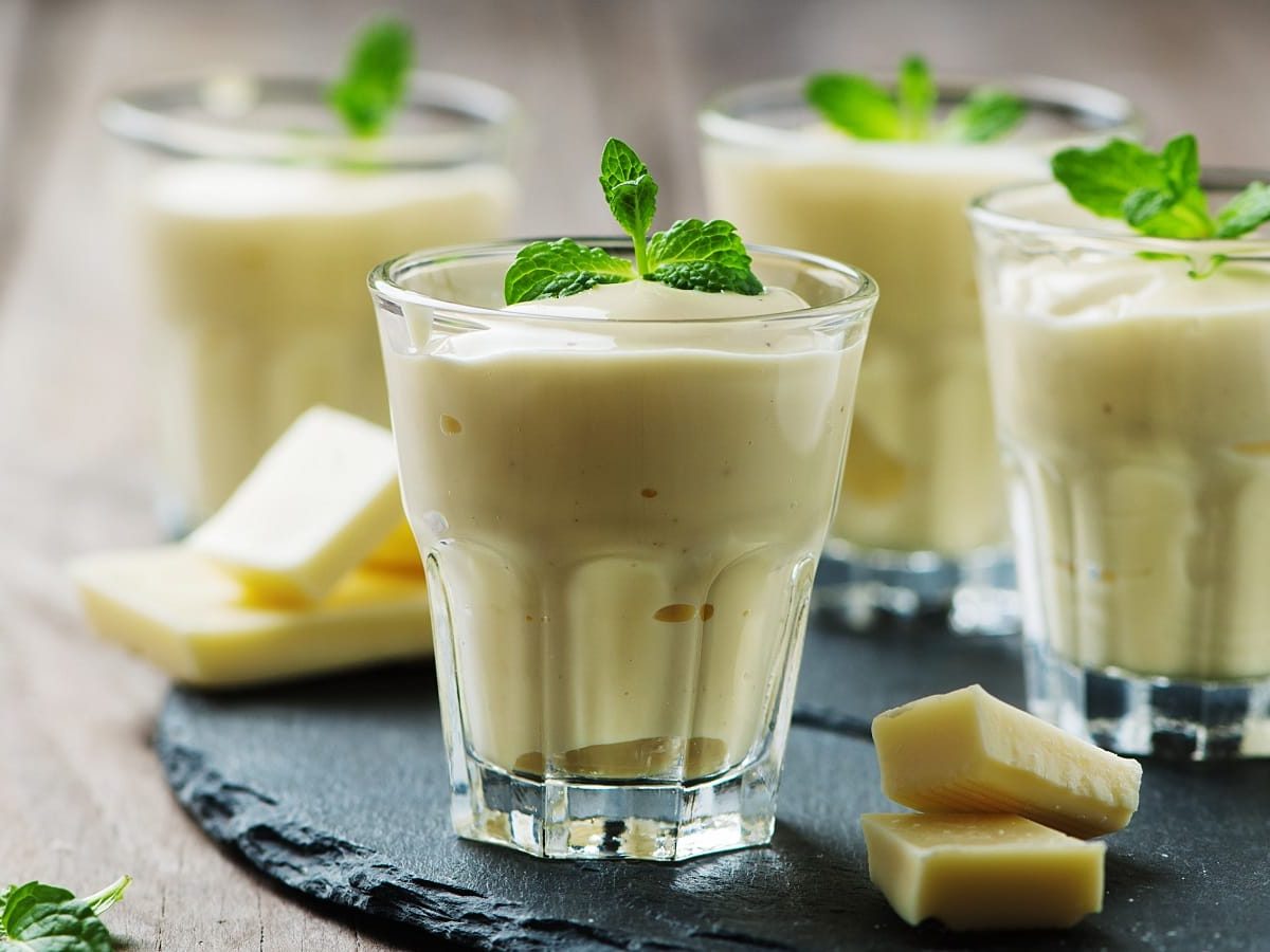 Vier Gläser mit Weiße-Schokoladen-Mousse auf einem Schiefer-Tablett.