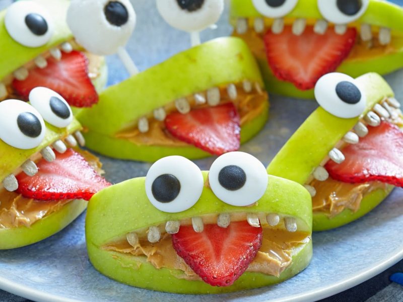 Mehrere gesunde Apfel-Monsterchen auf einem Teller vor blauem Hintergrund.