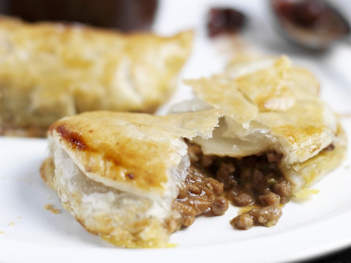 Tourtière-Pastete, bestehend aus Blätterteig und einer Hackfleischfüllung, aufgeschnitten serviert auf einem weißen Teller.