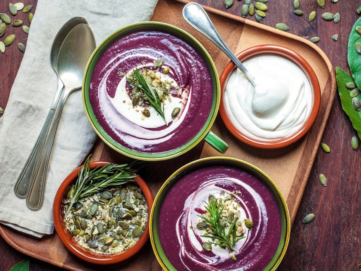 Zwei Schüsseln Kartoffelsuppe mit roter Bete garniert mit Kernen, Rosmarin und Joghurt. Draufsicht.